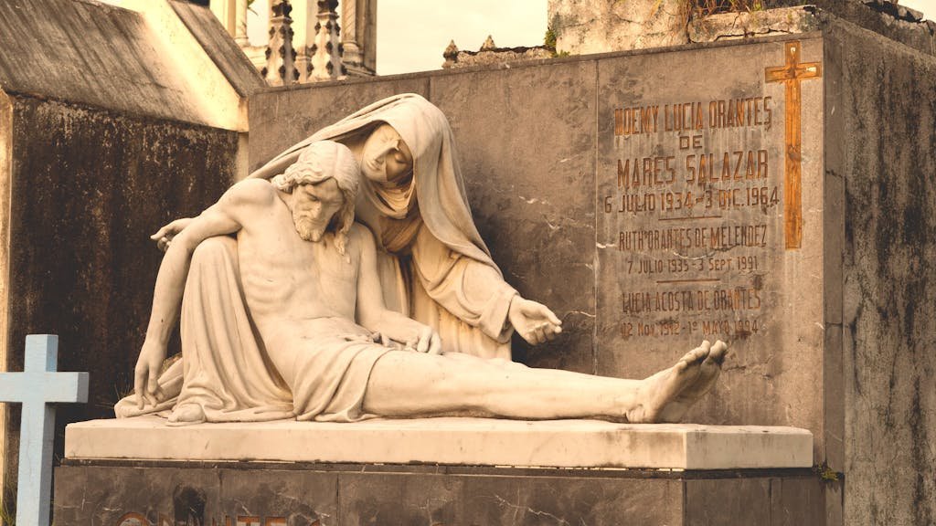 A weathered statue depicting a somber religious scene in a cemetery setting.