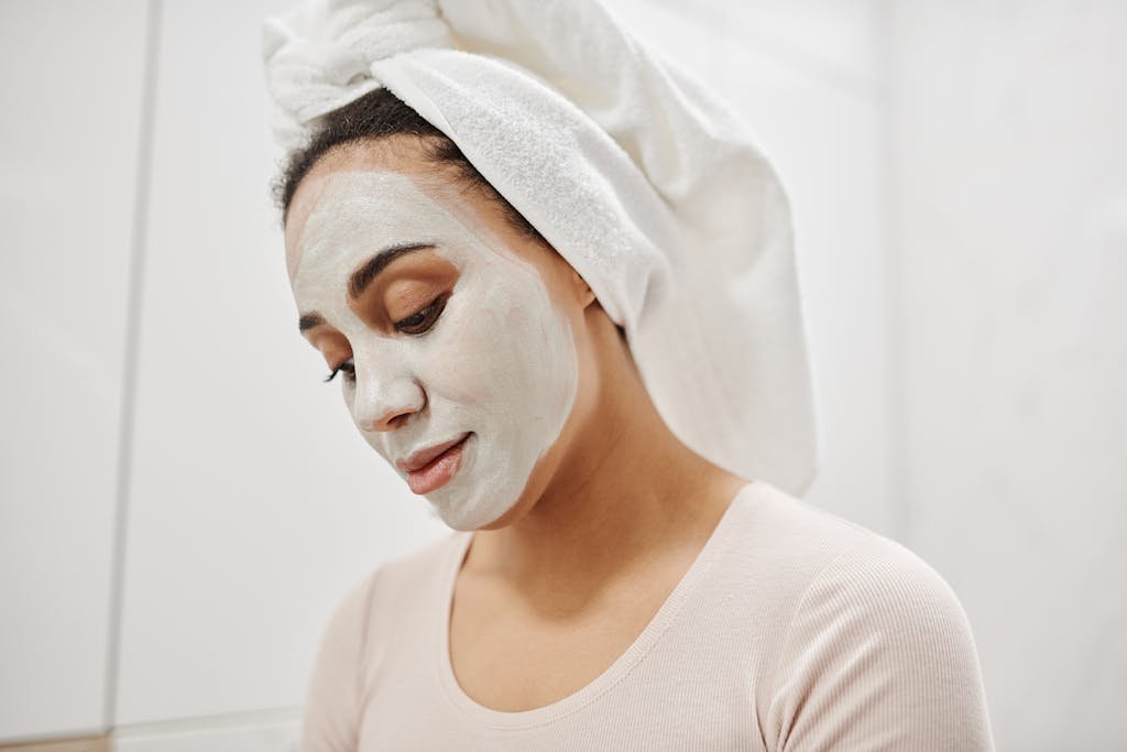 A woman indulges in self-care with a clay mask and towel wrapped on her head.