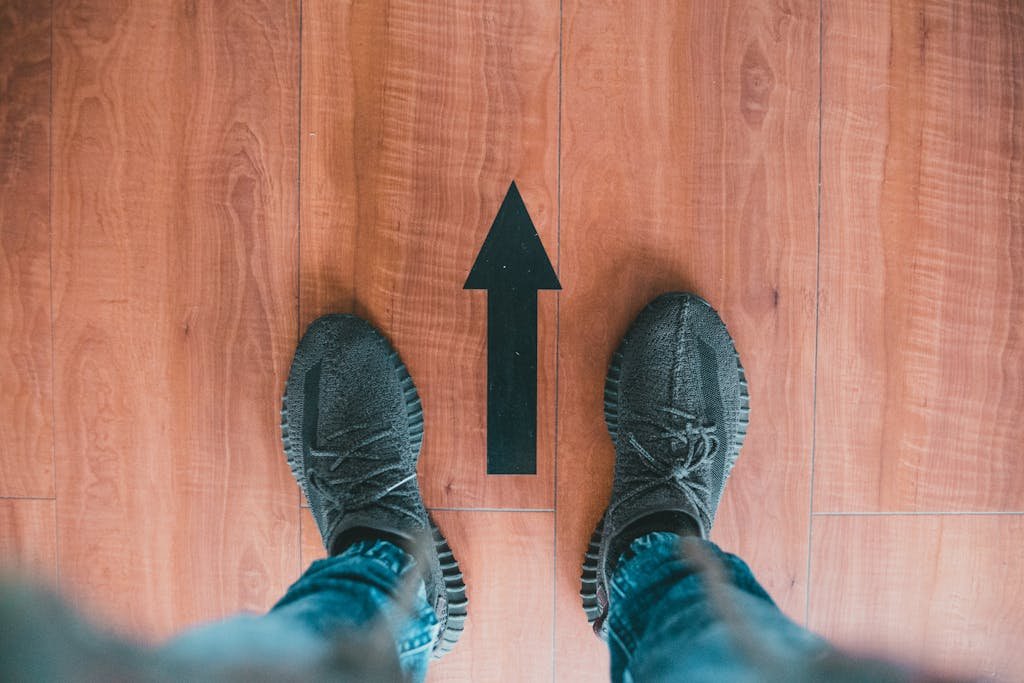 Casual sneakers viewed from above with a directional arrow on a wooden floor, suggesting movement.