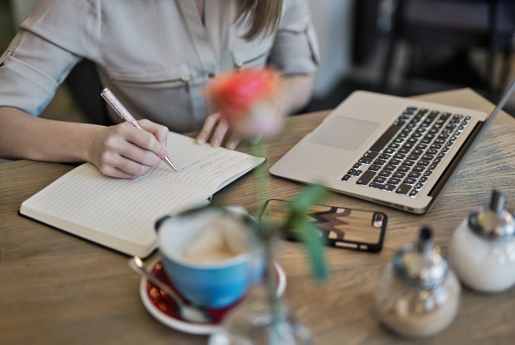 Woman writing in a notebook with a laptop and coffee cup for privacy policy on a desk. Ideal for workspace inspiration.
