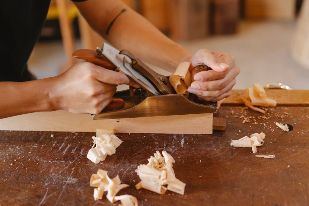 A carpenter skillfully using a hand plane to smooth a wooden plank in a workshop.
