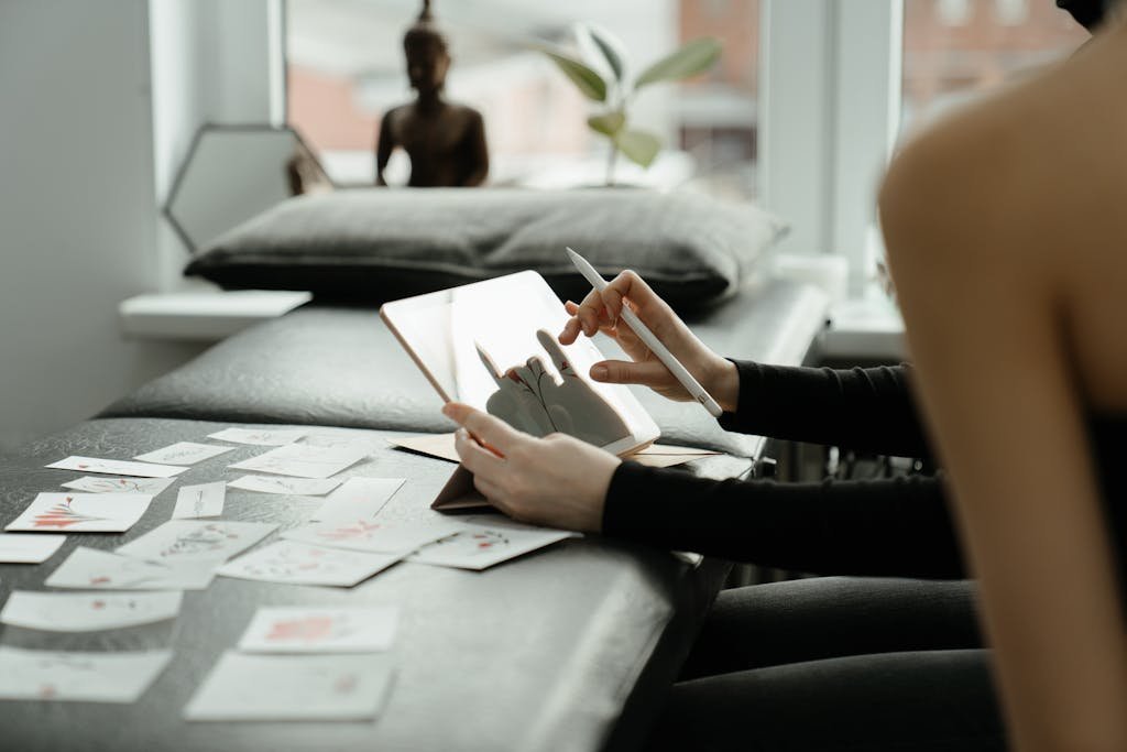 A person sketching tattoo designs on a tablet surrounded by sketches in a studio.