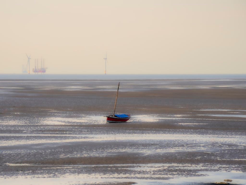A serene beach at West Kirby featuring a solitary boat and distant wind turbines under a misty sky.
