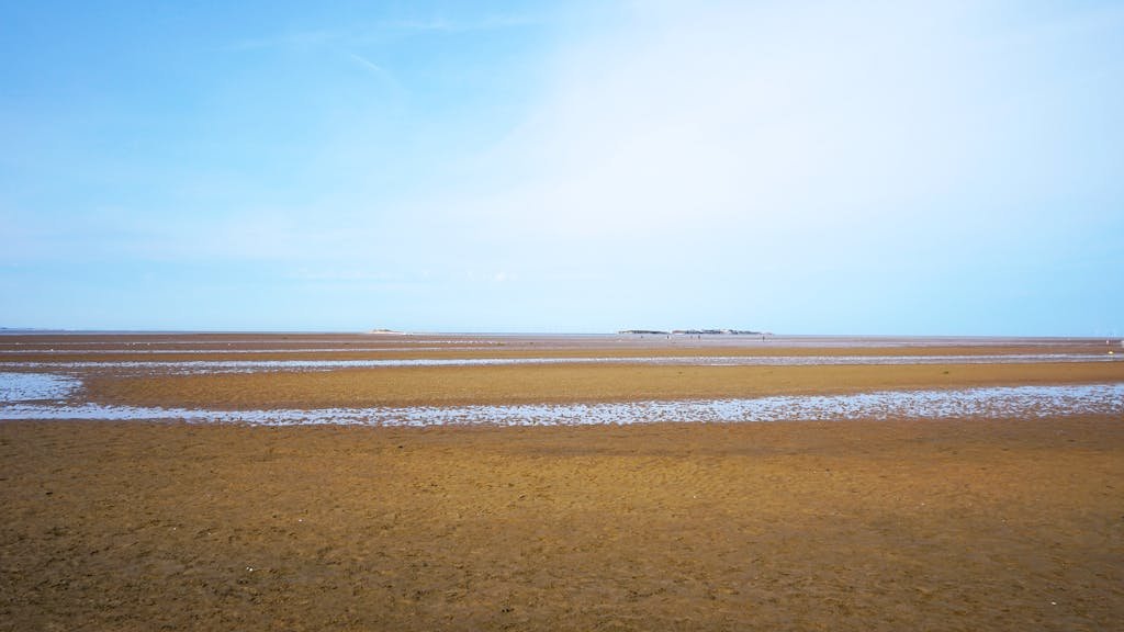A serene view of the sandy tidal flats in West Kirby, UK with blue sky.