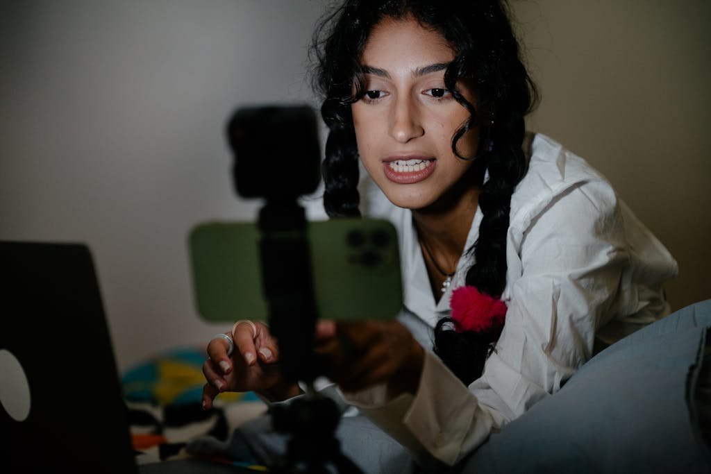 Explore Latest Tech Trends Today with braided hair records a video using her smartphone and laptop indoors.