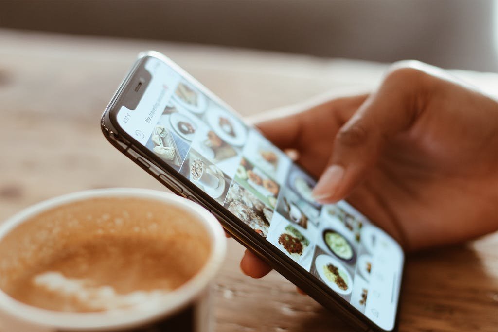 ClickUp App browsing social media photos on a smartphone next to a cup of coffee indoors.