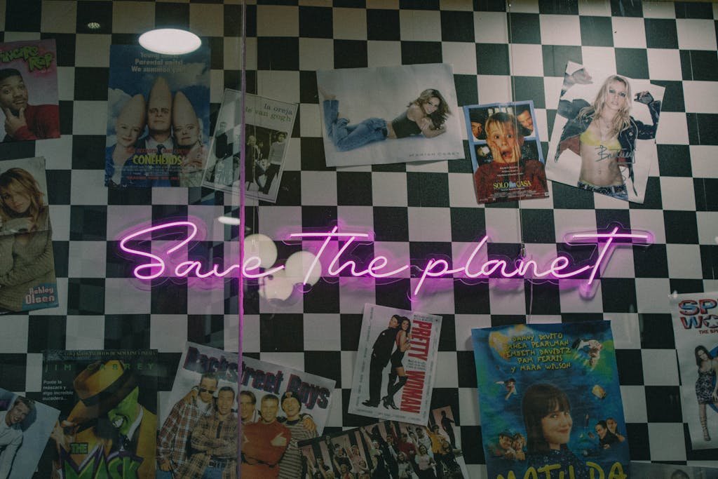 Neon sign with 'Save The Planet' on a checkerboard wall, surrounded by vintage posters.