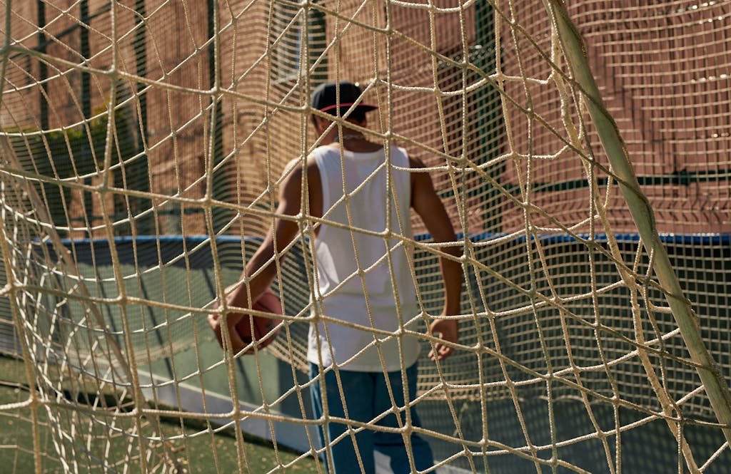 Person holding a basketball behind a net on a city court, showcasing urban sports culture.