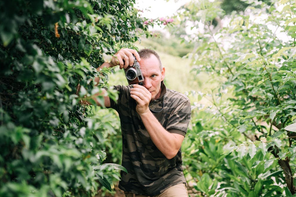 Seekde in camo shirt capturing nature photos amid lush vegetation.