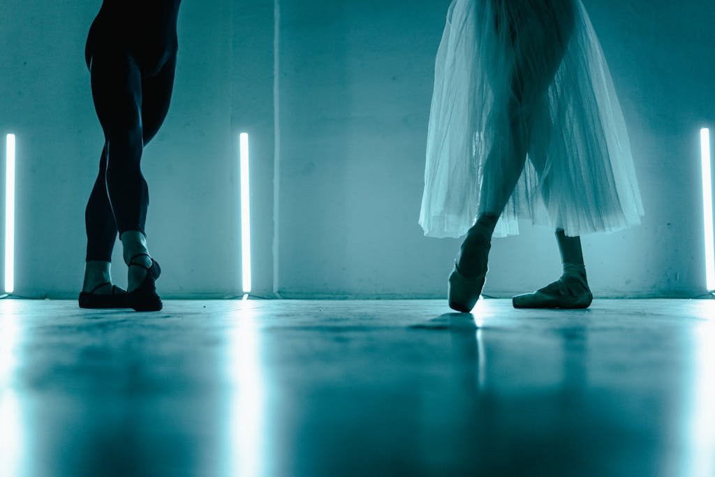 Two ballet dancers pose gracefully in a dimly lit studio, showcasing elegance and poise.