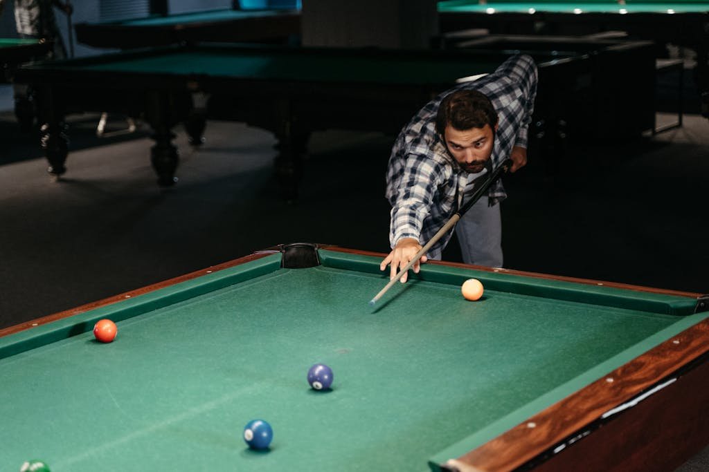 Manual Settings HSSGameStick focused on making a shot at a billiard table in a moody, dimly lit pool hall setup.
