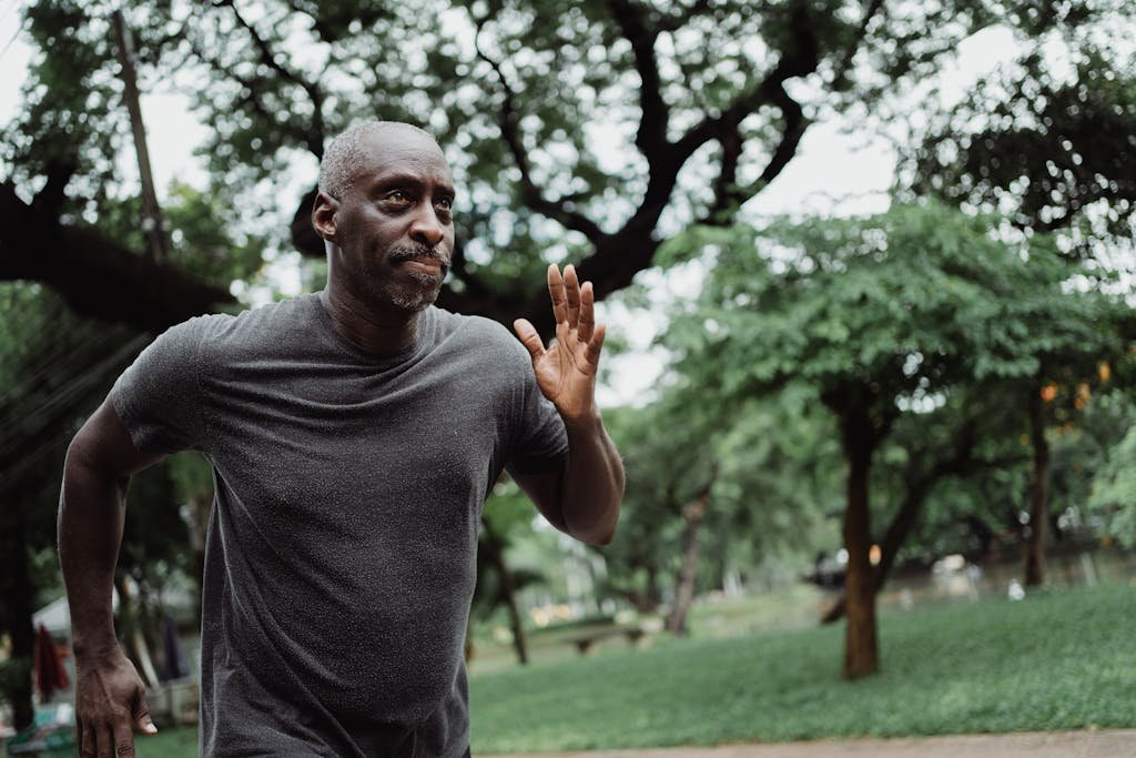 Senior man running through a lush green park, focused on fitness and wellbeing outdoors.