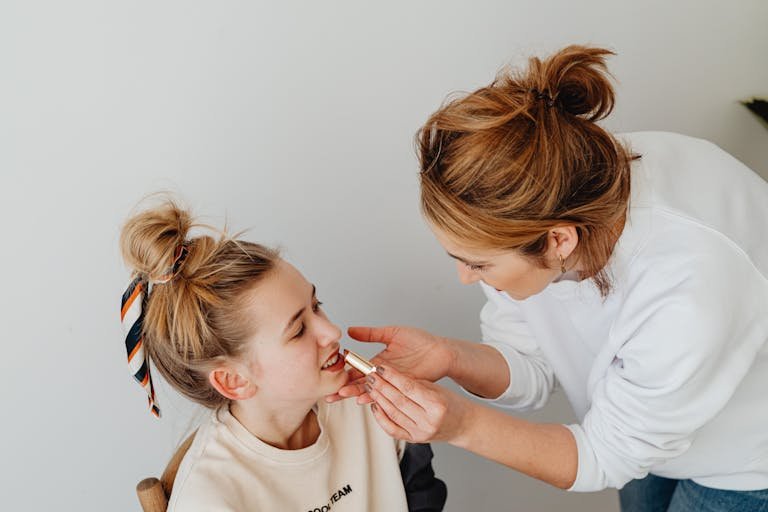 A Natural Beauty Tips bonding with her daughter by applying lipstick in a cozy indoor setting.