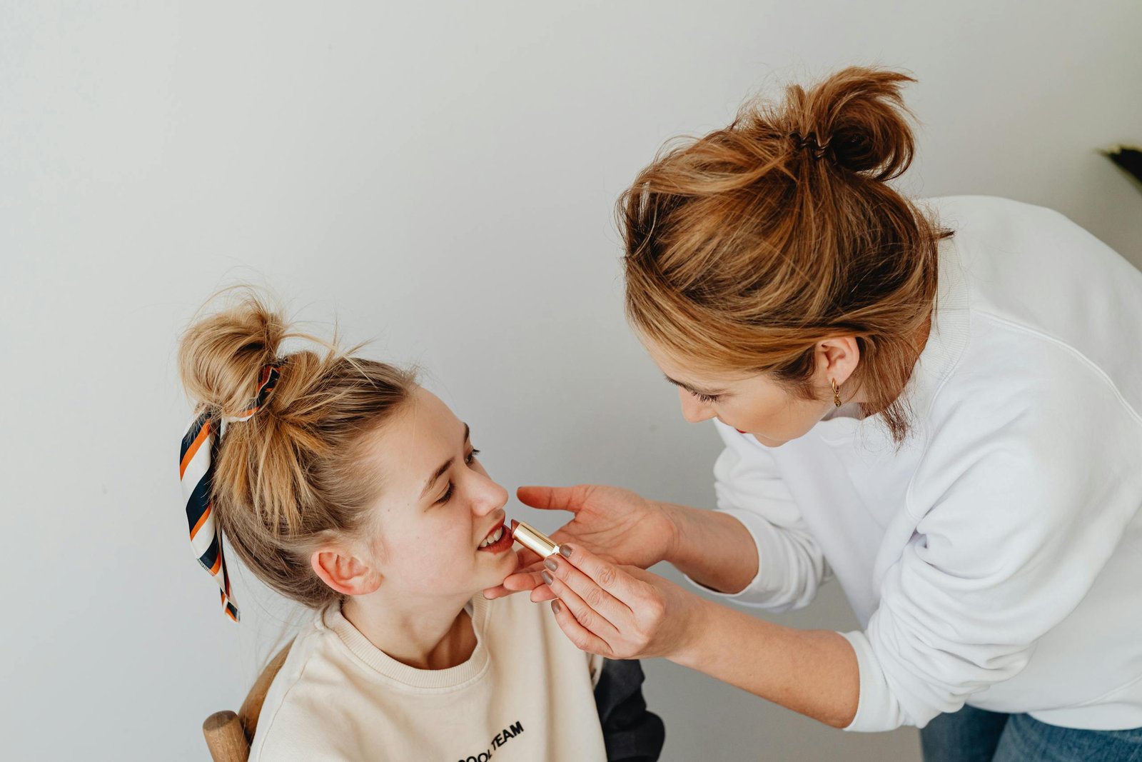 A Natural Beauty Tips bonding with her daughter by applying lipstick in a cozy indoor setting.