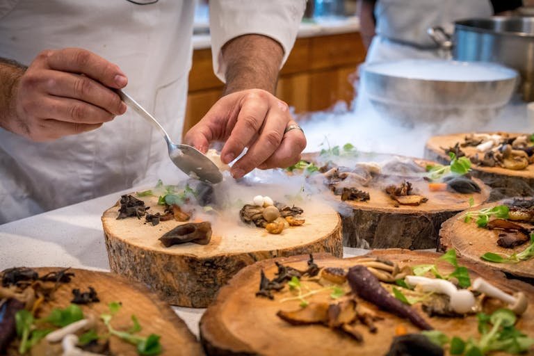 ClickUp Mastery plating a gourmet dish with mushrooms and greens on wood slices.