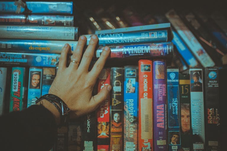 A hand S.S. Rajamouli's Movies for a classic VHS tape from a colorful vintage collection indoors.
