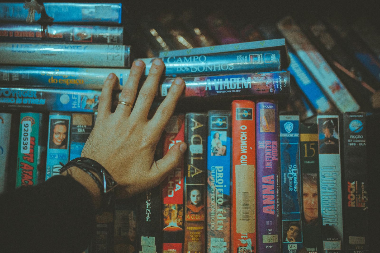 A hand S.S. Rajamouli's Movies for a classic VHS tape from a colorful vintage collection indoors.