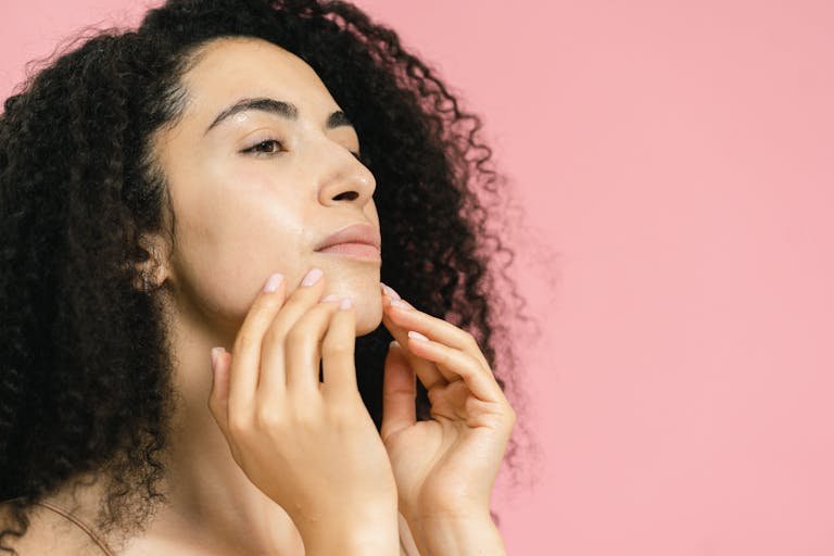 Organic Beauty Tips curly hair touches her face, set against a pastel pink background.