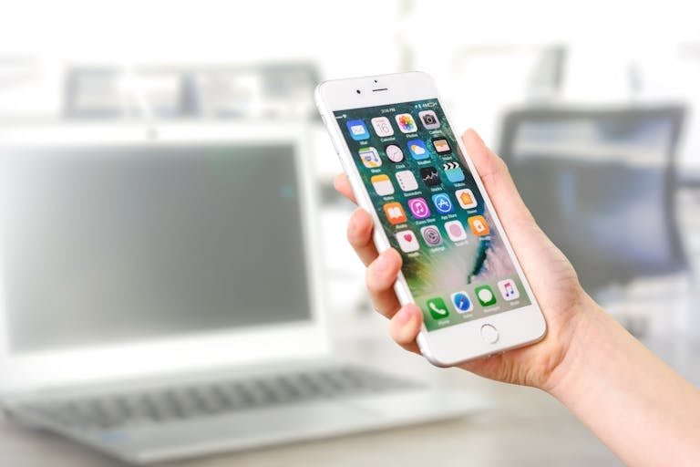ClickUp Careers view of a smartphone displaying apps, held by a hand, with a blurred laptop in the background.