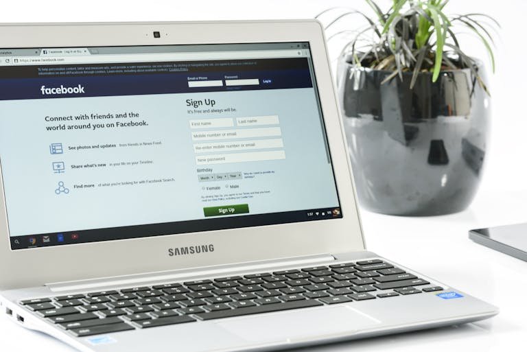 ClickUp Login Samsung laptop showing Facebook sign-up page next to a potted plant. Ideal for technology themes.