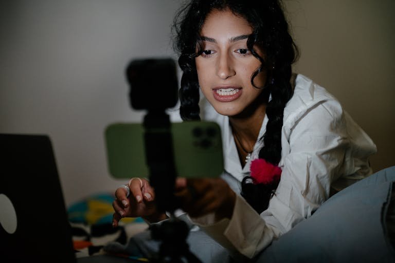 Explore Latest Tech Trends Today with braided hair records a video using her smartphone and laptop indoors.