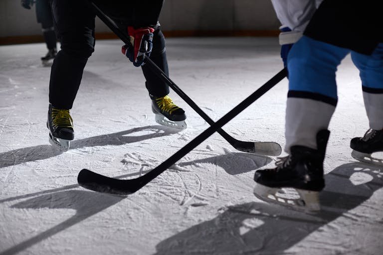 Manual Settings HSSGameStick hockey players battling for puck during an intense face-off on a lighted ice rink.