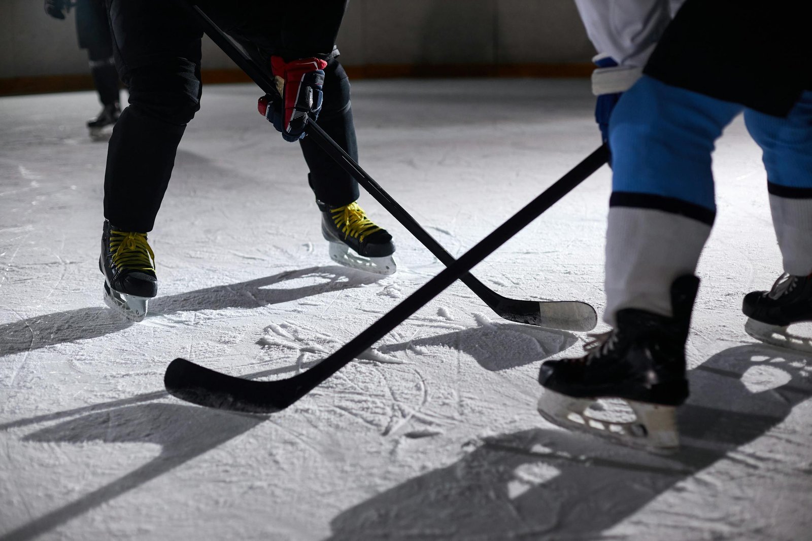 Manual Settings HSSGameStick hockey players battling for puck during an intense face-off on a lighted ice rink.